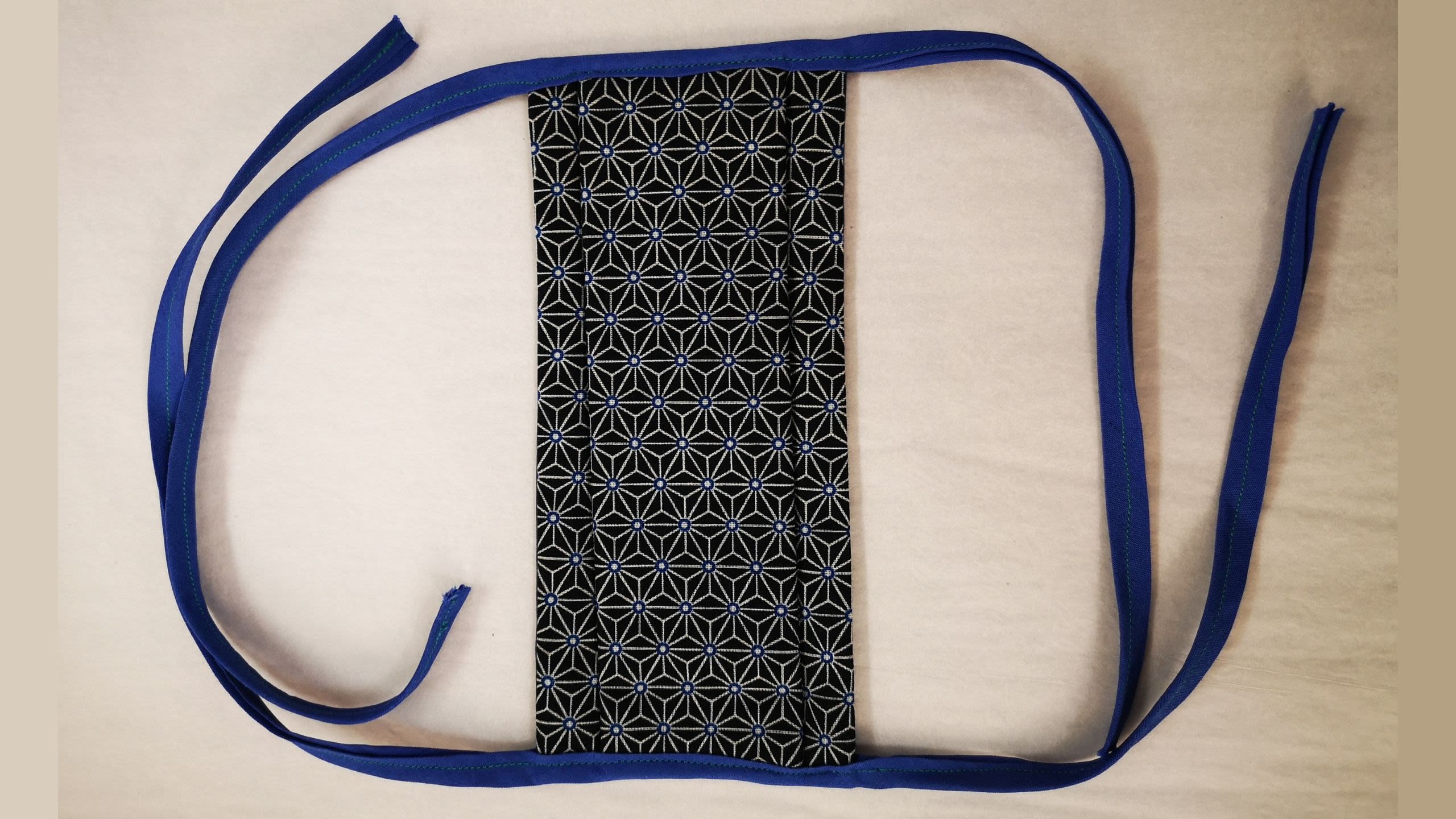 Handmade face covering of black patterned cotton with blue tie straps (Inv 18497)